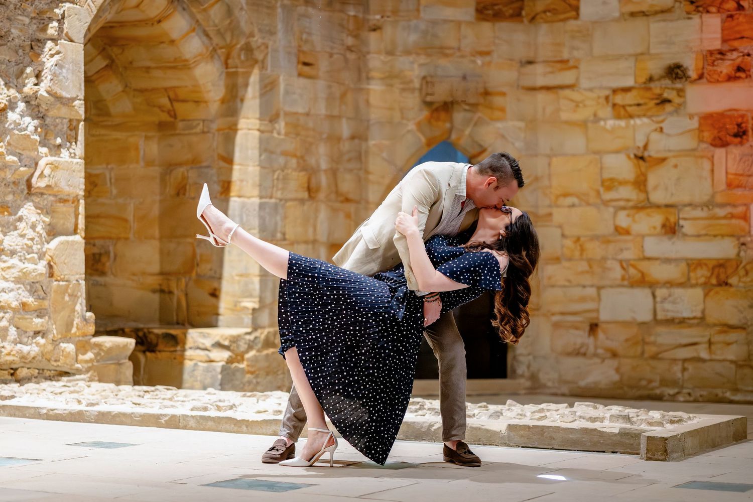 Couple dancing a romantic tango dip pose in front of ancient stone ruins during an outdoor engagement photo shoot.