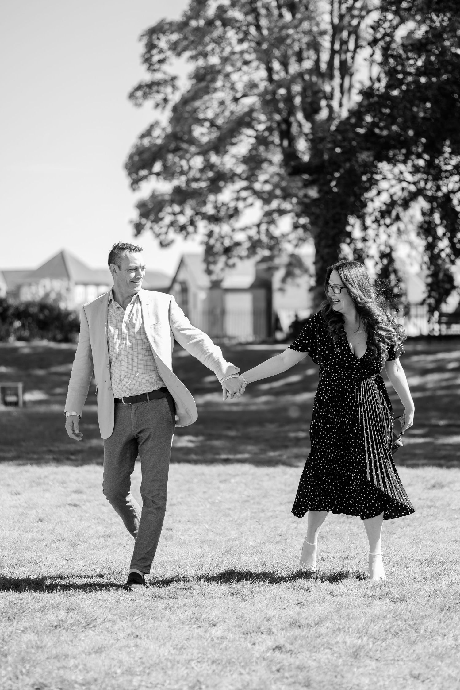 Black and white photo of a couple holding hands and walking together in a sunny park.