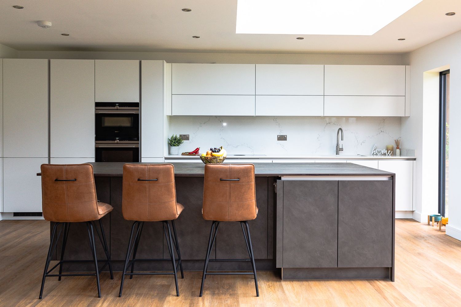 Sleek modern kitchen featuring concrete-style island, tan leather bar stools, and skylight.