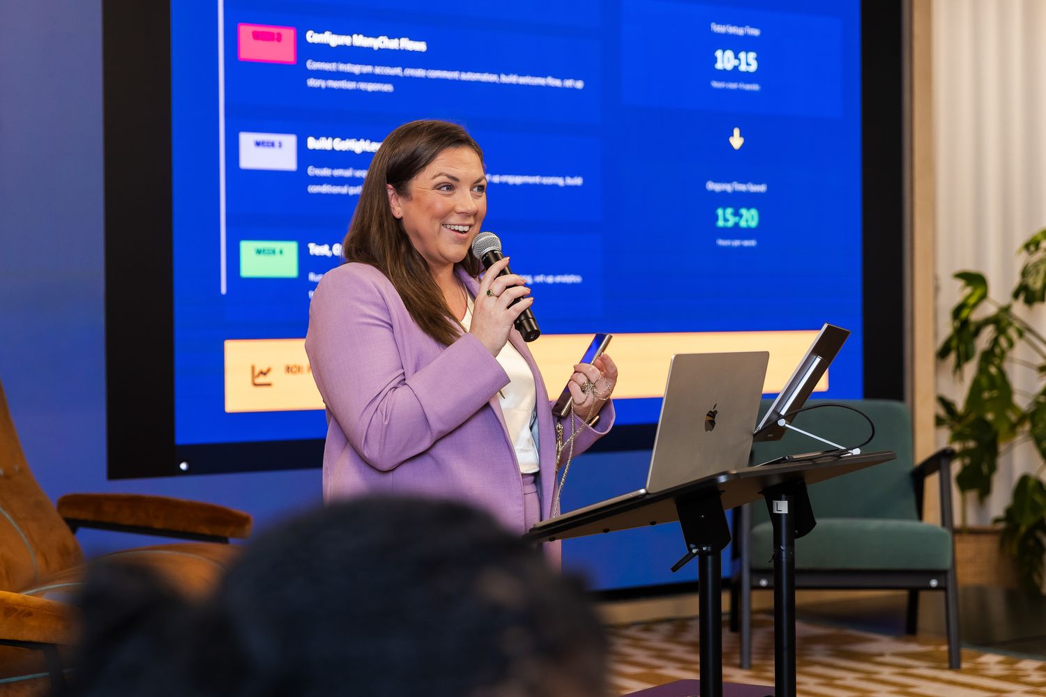 Woman in lavender blazer presents data on screen at professional business conference.