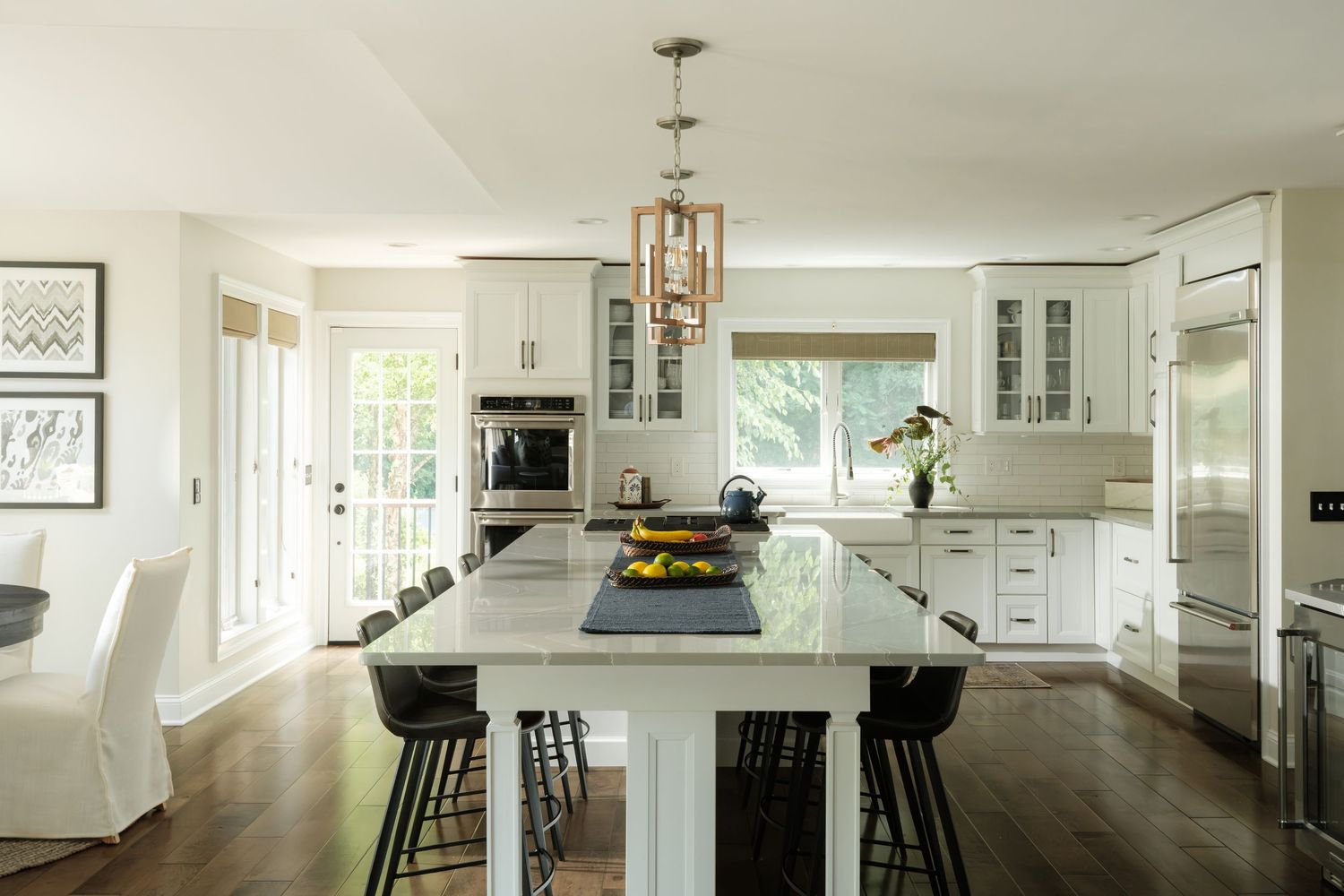 Bright white kitchen with marble island, black bar stools, pendant lighting, and dark hardwood floors.