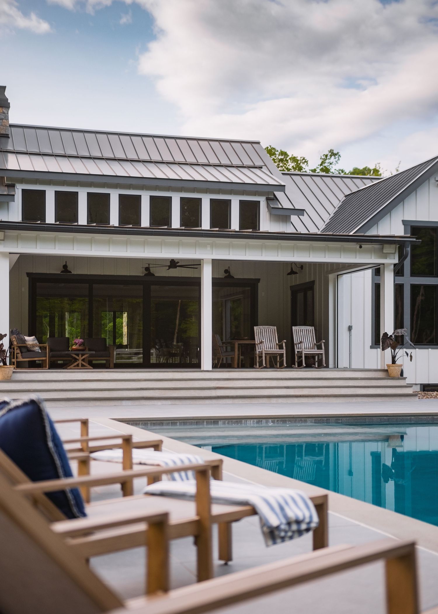 Modern farmhouse exterior with swimming pool, lounge chairs, and covered porch area.