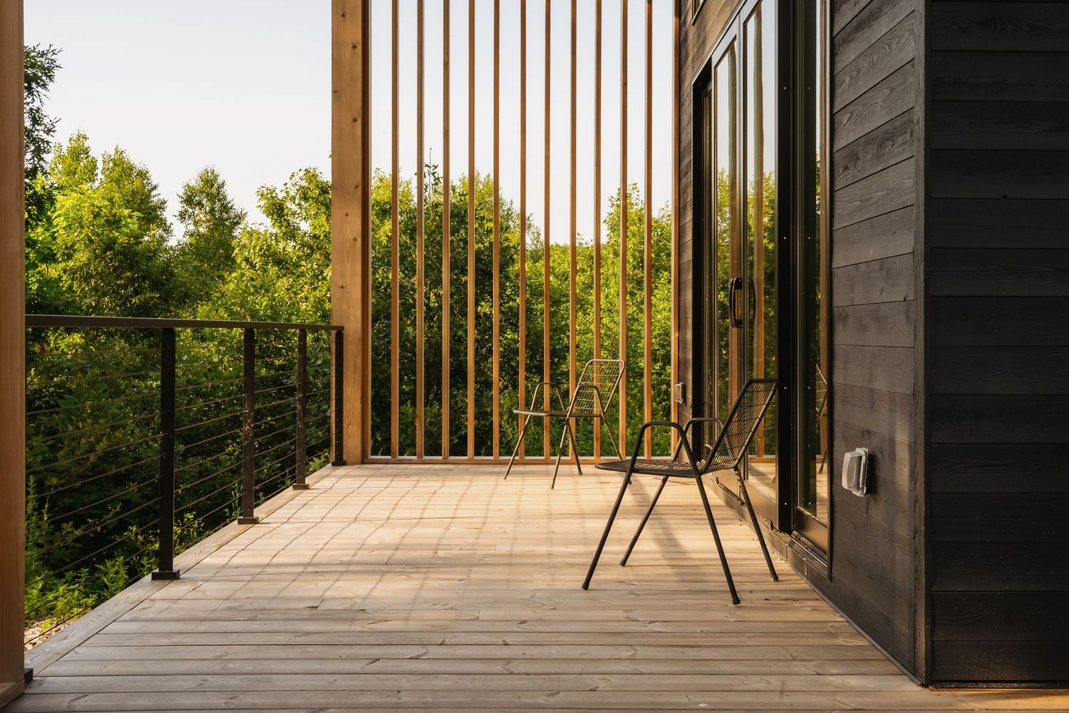 Wooden deck with vertical metal railings and outdoor chair overlooking trees.