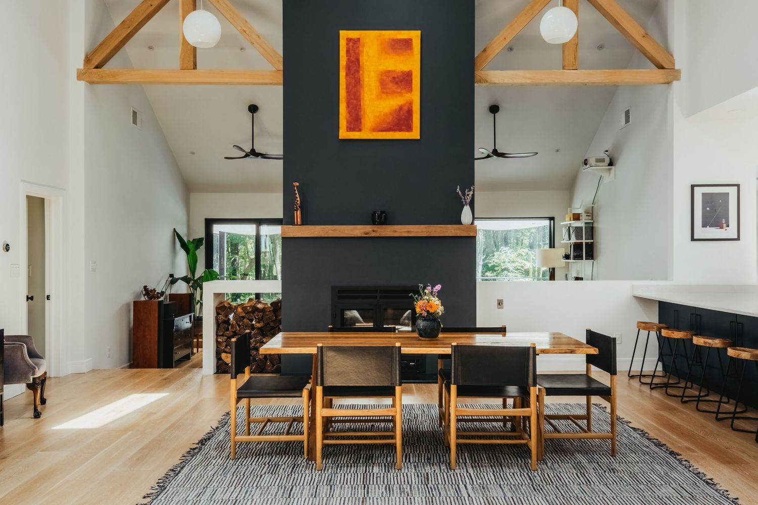 Modern open-plan living room with wood furniture and dark accent walls features pendant lighting and high ceilings.