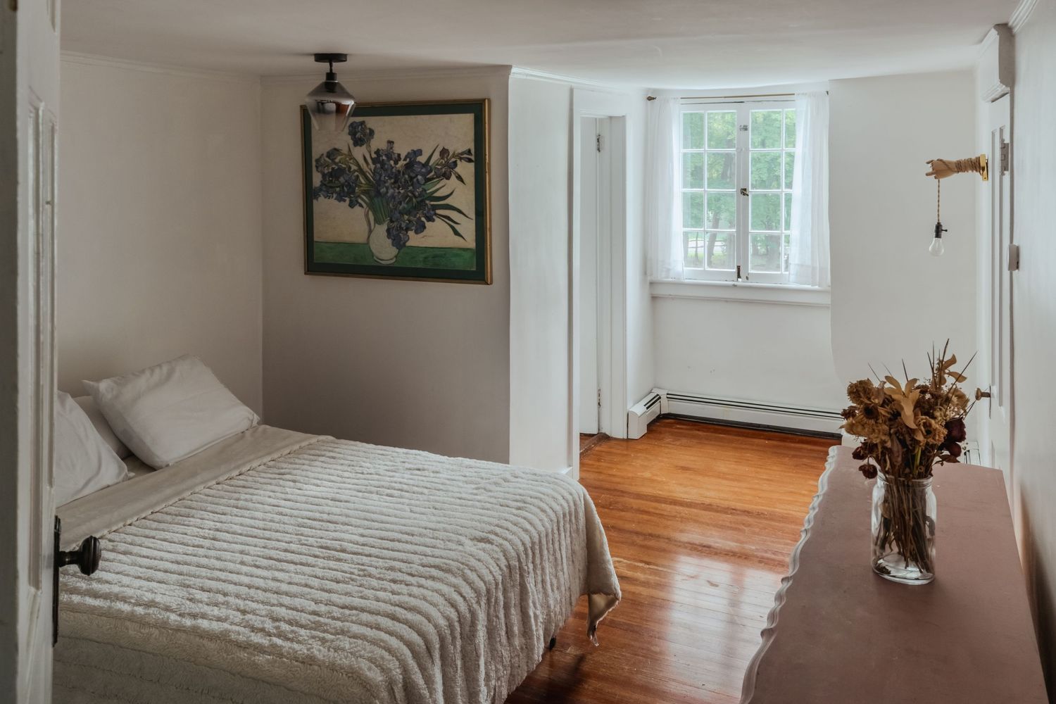 A panoramic view of a bright bedroom with white walls, hardwood floors, and multiple windows letting in natural light.