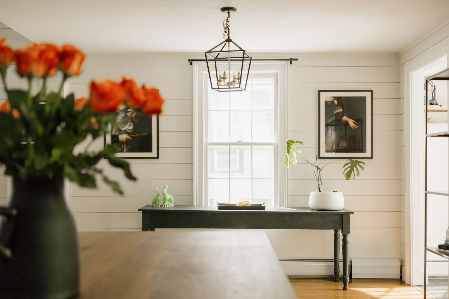 Elegant dining room with shiplap walls, lantern pendant light, console table, and orange tulips in foreground.