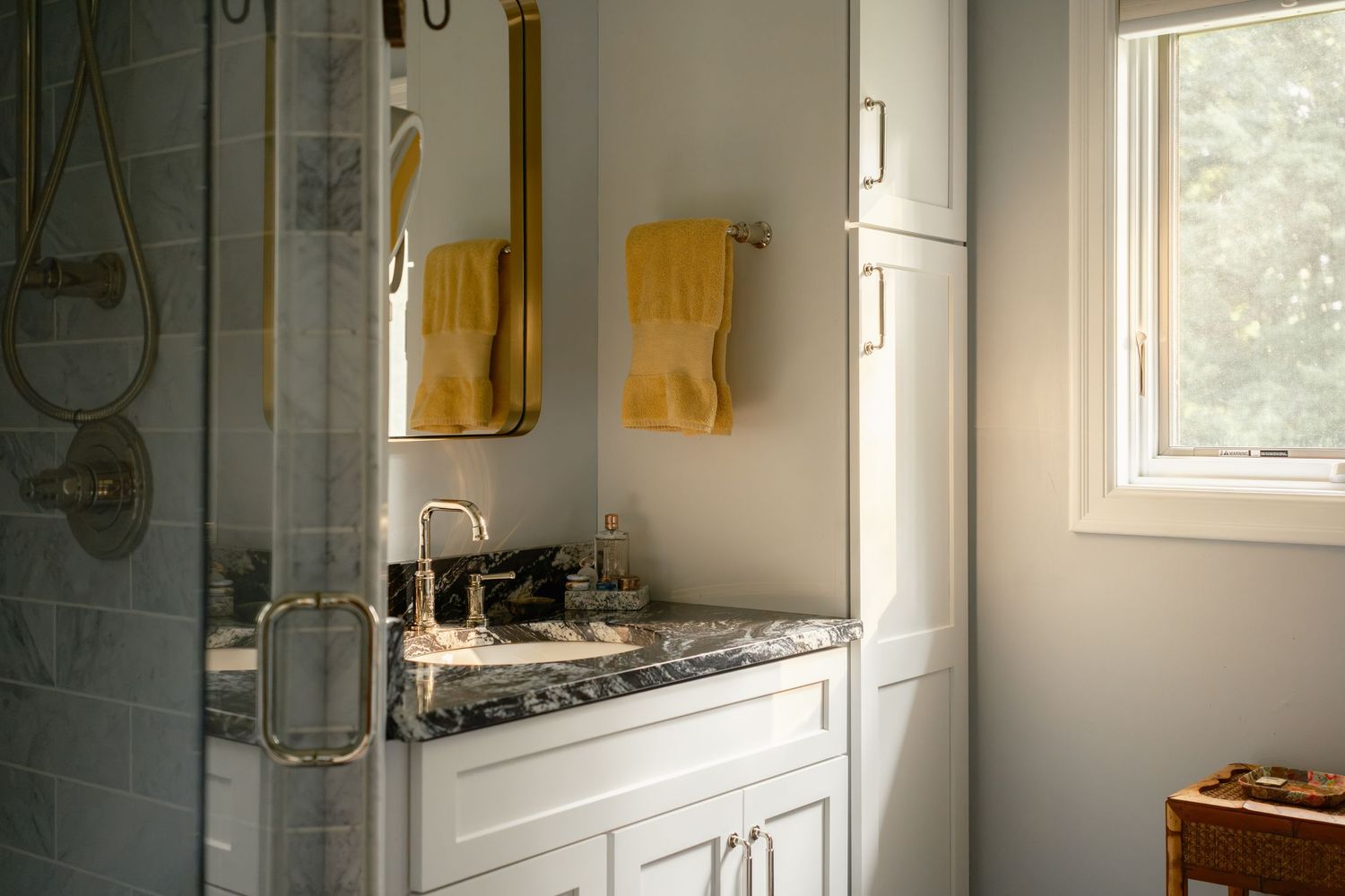 Elegant bathroom with white cabinets, dark marble countertop, gold fixtures, and glass shower.