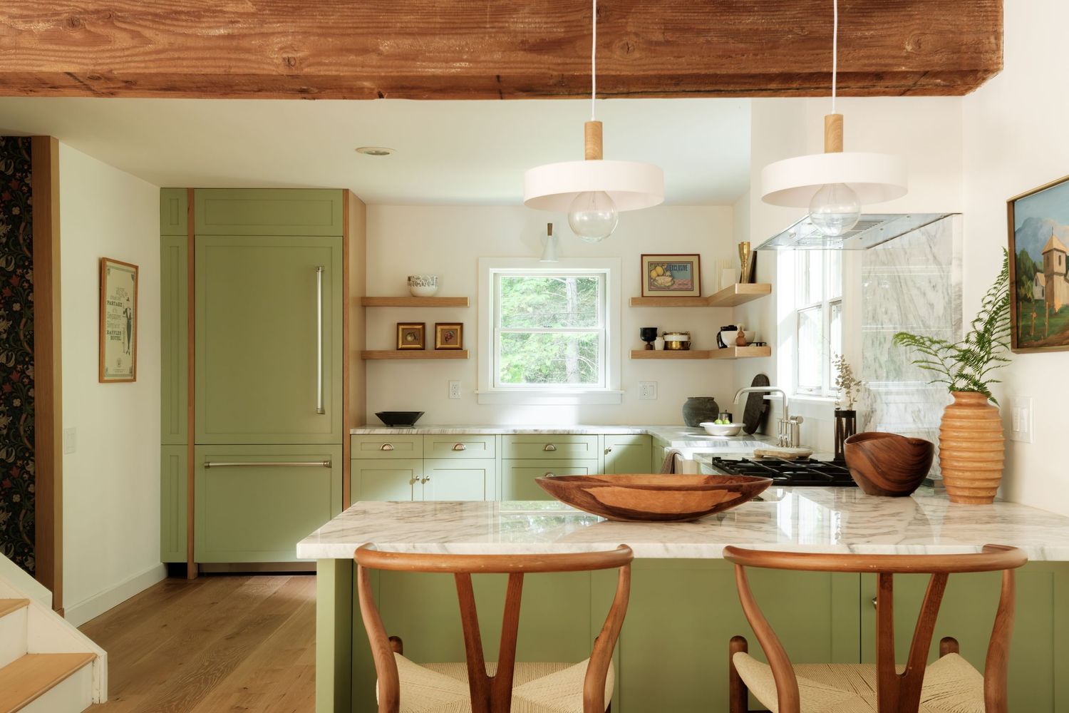 Sage green kitchen with marble island, pendant lights, open shelving, and warm wood accents in a bright, modern space.