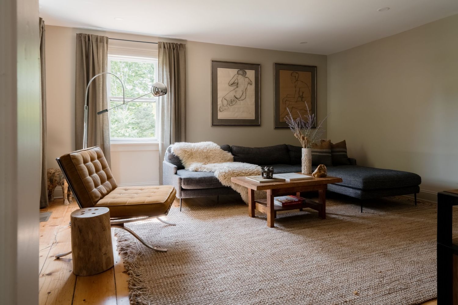 Cozy neutral living room with jute rug, dark sofa, leather chair, wood coffee table, and natural light from window.