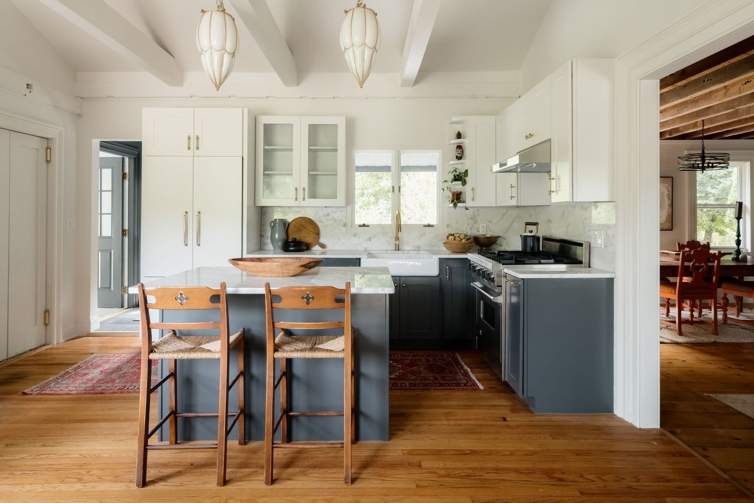 Modern farmhouse kitchen with two-tone gray and white cabinets, wood bar stools, hardwood floors, and pendant lights.