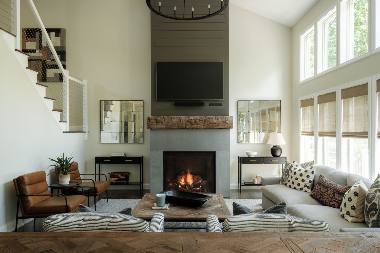 Modern living room with stone fireplace, large sectional sofa, leather chairs, and tall windows with natural light.