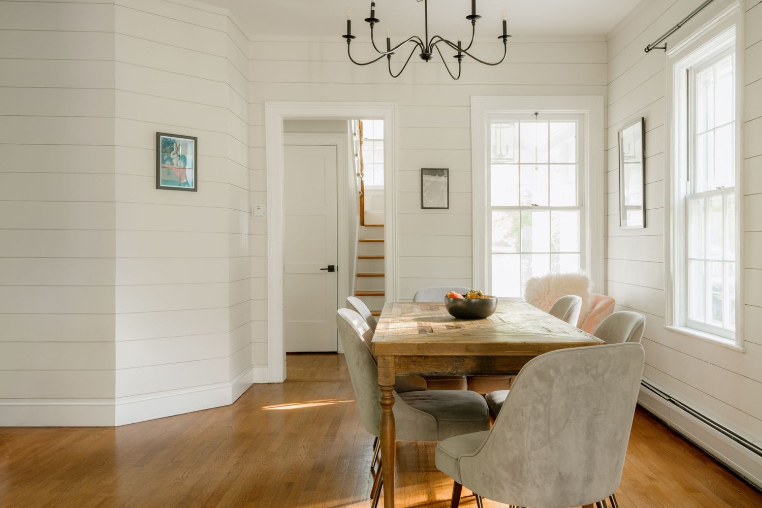 Bright dining room with shiplap walls, wood table, velvet chairs, chandelier, and hardwood floors.