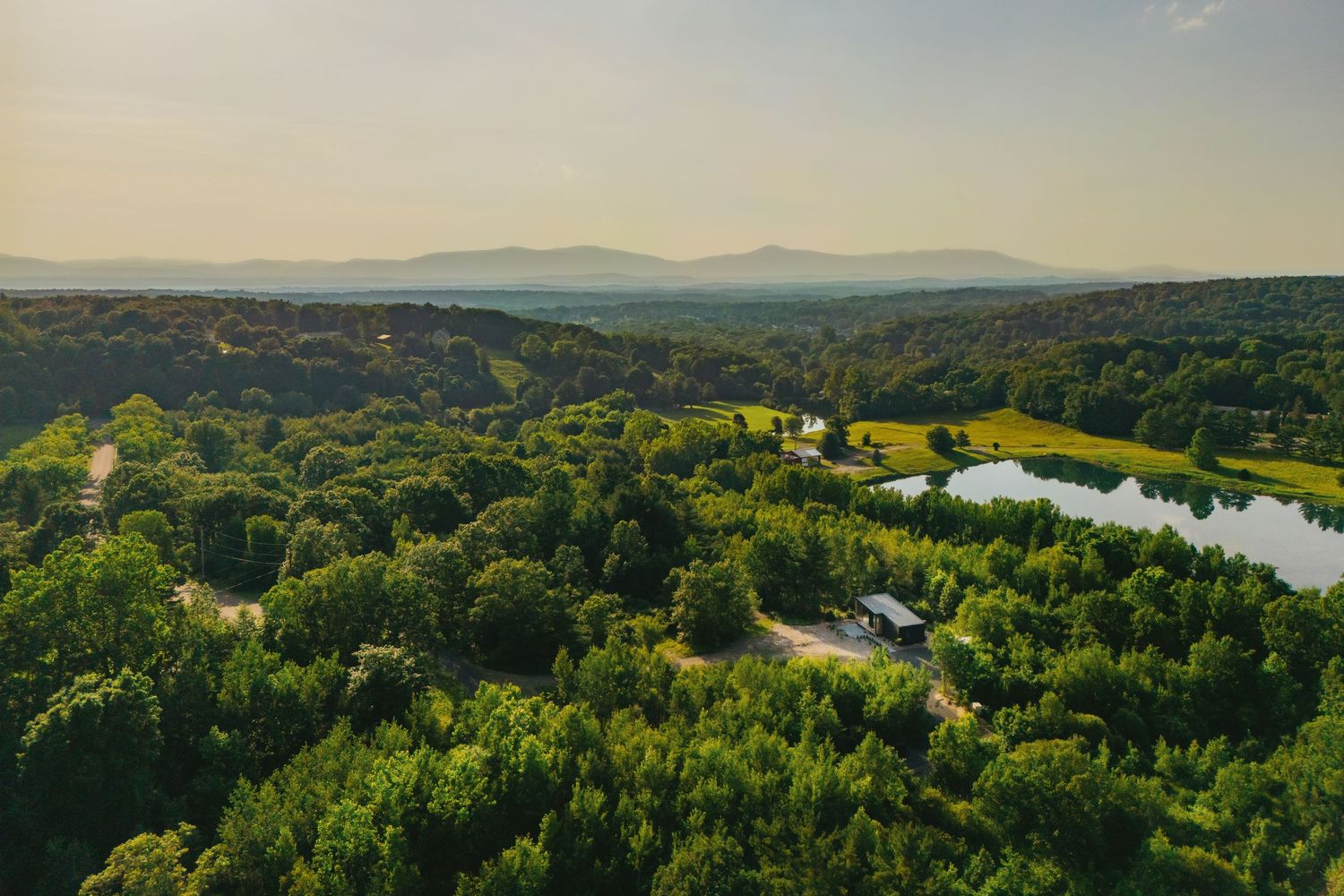 Aerial view of lush green countryside landscape with a serene lake nestled among rolling hills.