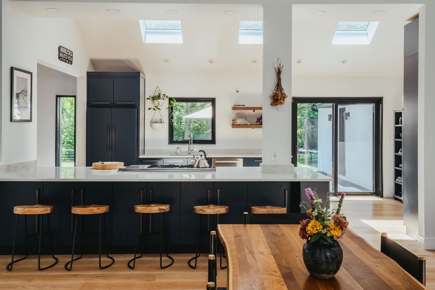 Modern kitchen interior with black island counter, wooden bar stools, skylights and hardwood flooring.