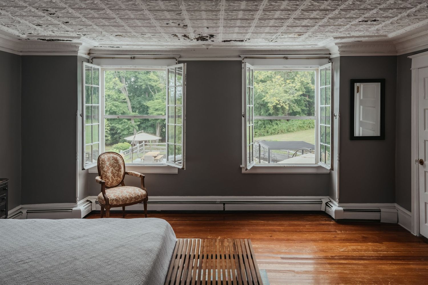 Modern open concept room with gray walls, hardwood floors and multiple windows offering natural light.