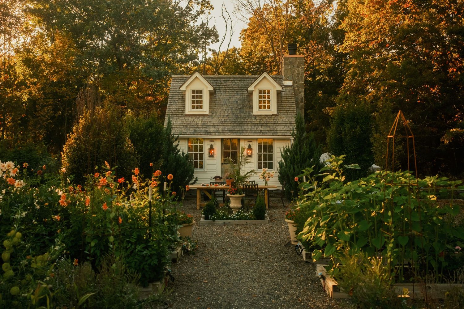 Charming cottage with dormers nestled among autumn trees at golden hour.
