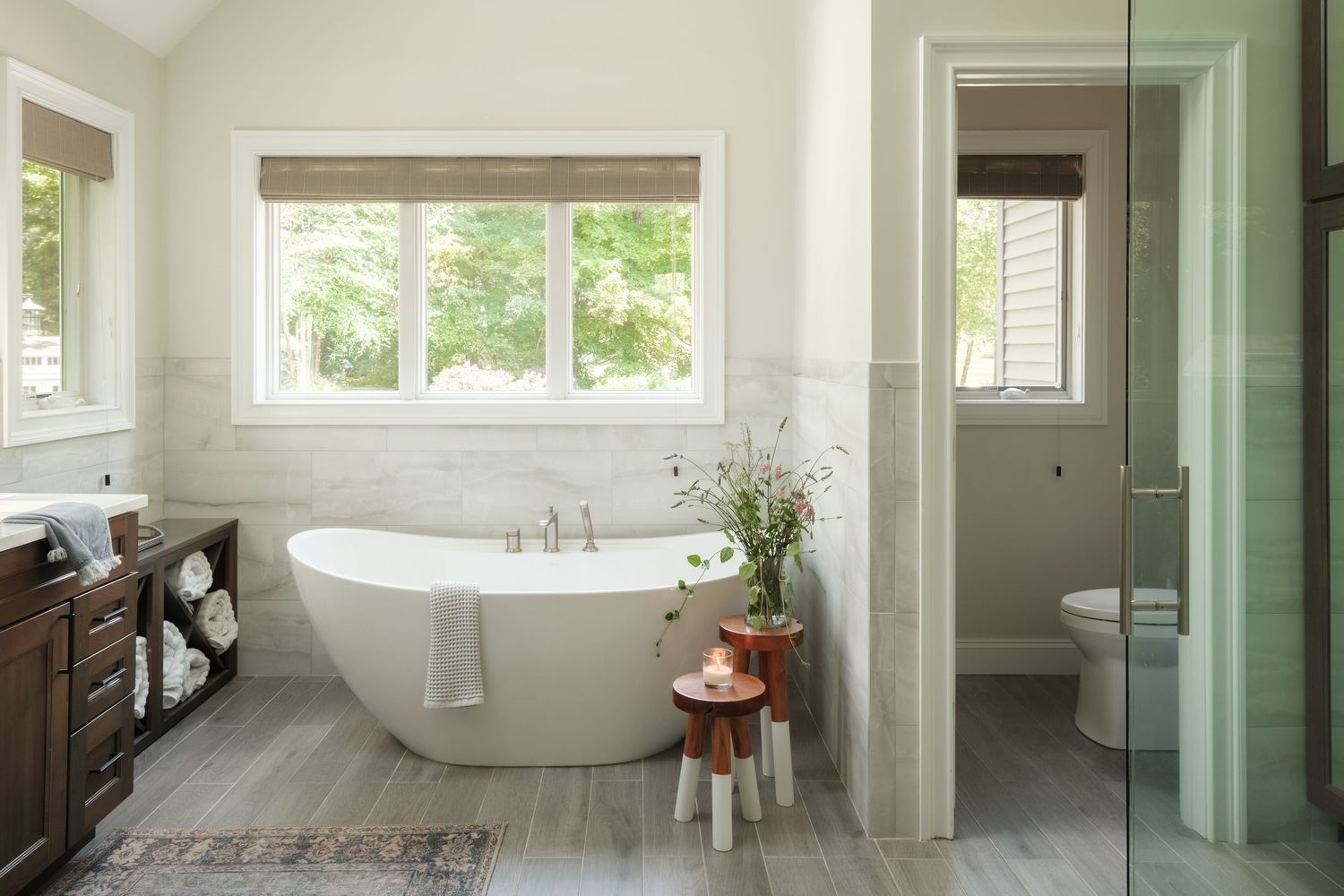Bright master bathroom with freestanding soaking tub, marble tile, wood vanity, and glass shower enclosure.