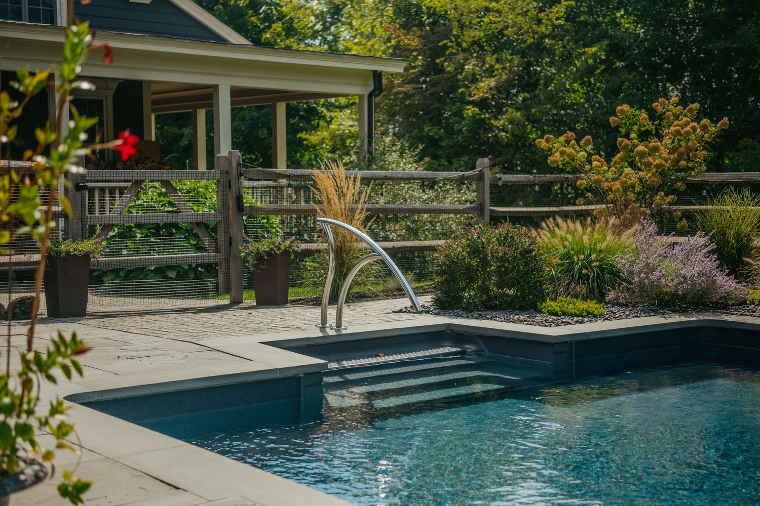 Modern swimming pool with curved fountain feature and landscaped garden surrounding a paved patio area.