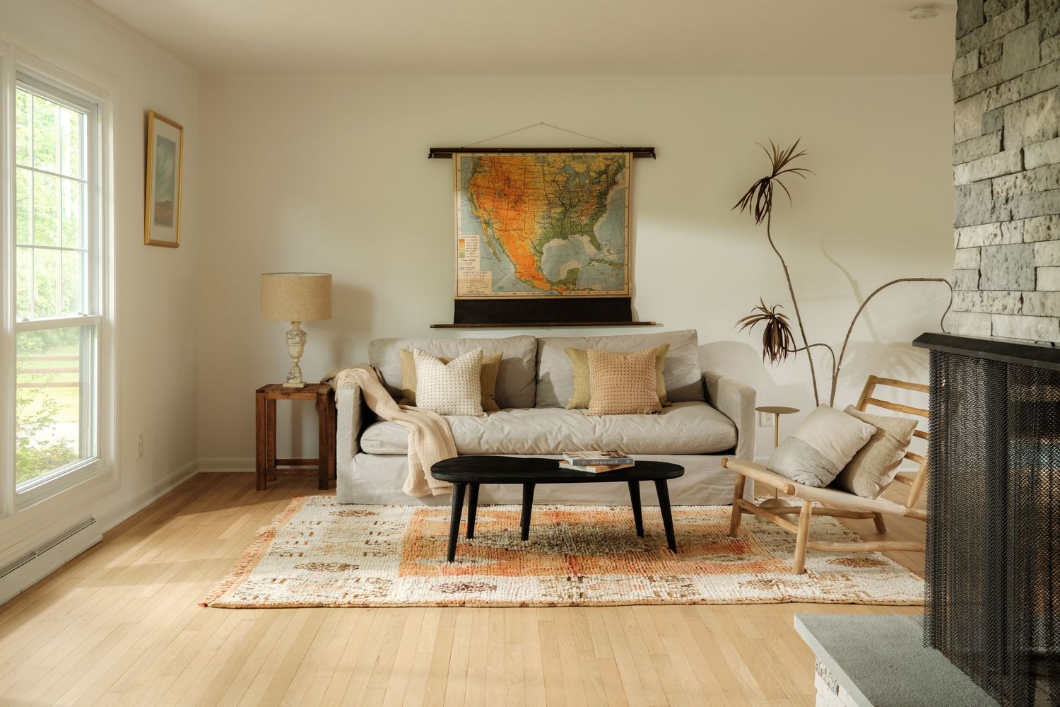 Cozy living room with a neutral sofa, vintage map wall art, wood coffee table, and patterned rug on light hardwood floors.
