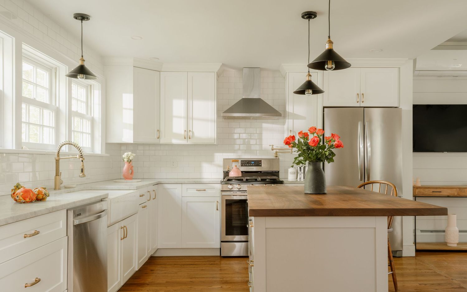 Bright white kitchen with gold hardware, black pendant lights, stainless appliances, and a butcher block island centerpiece.