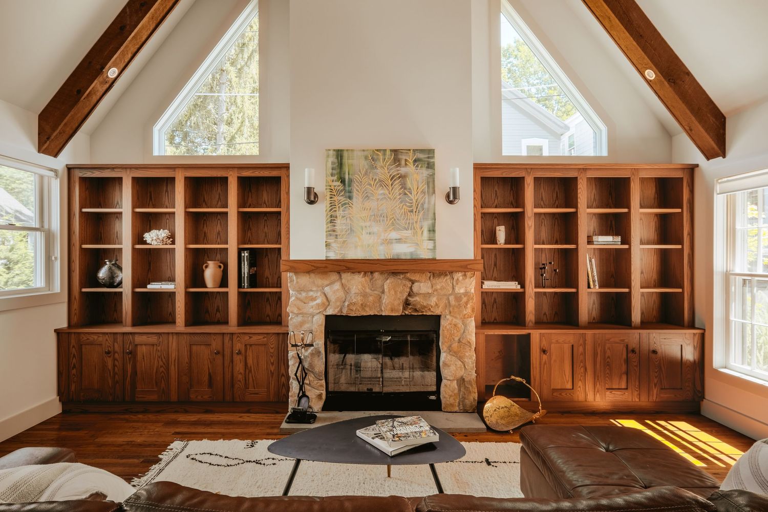 Cozy living room interior with wooden built-in shelving, stone fireplace, and vaulted ceiling with natural light.