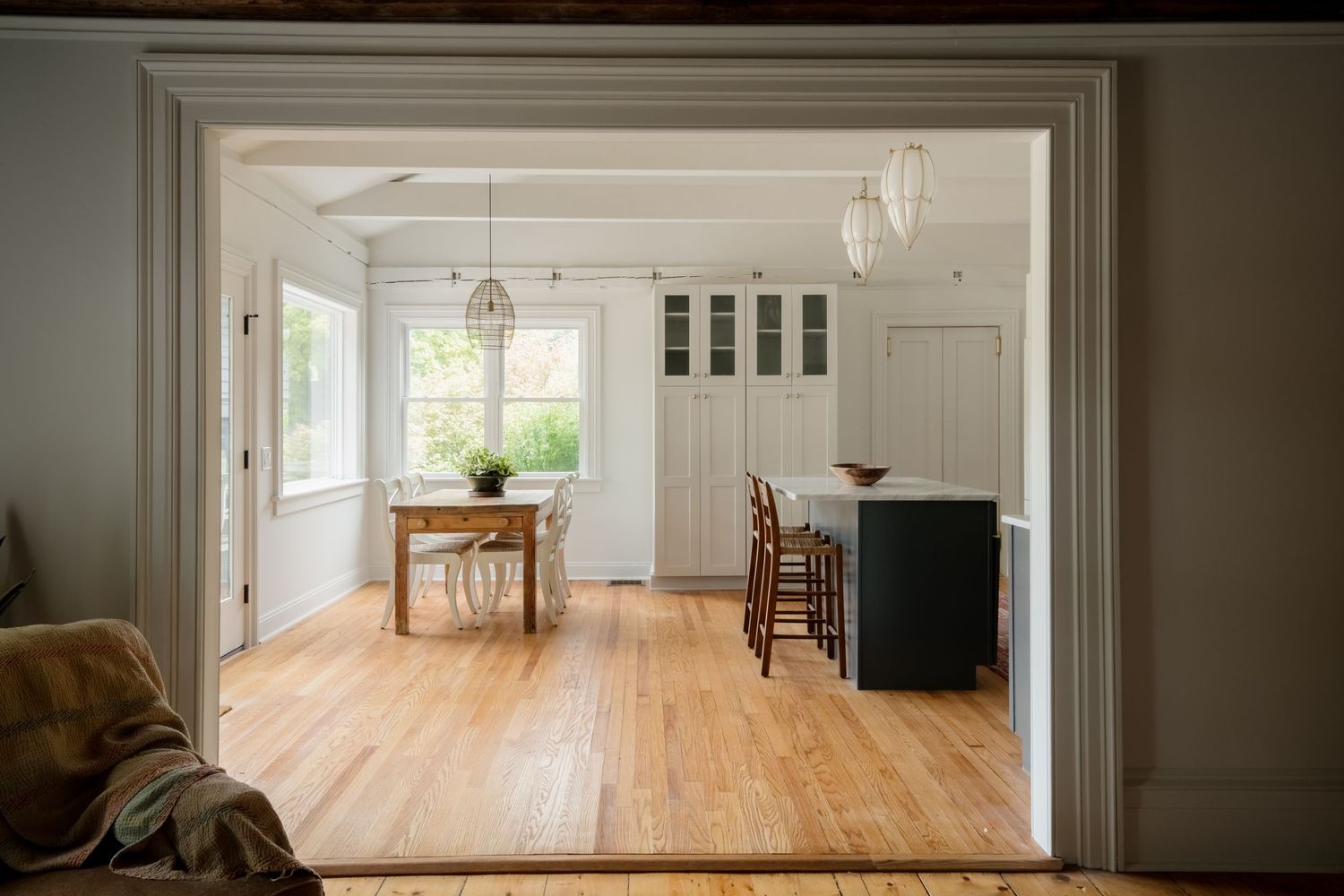 Bright open-plan kitchen and dining area with light hardwood floors, white cabinetry, dark island, and pendant lights.