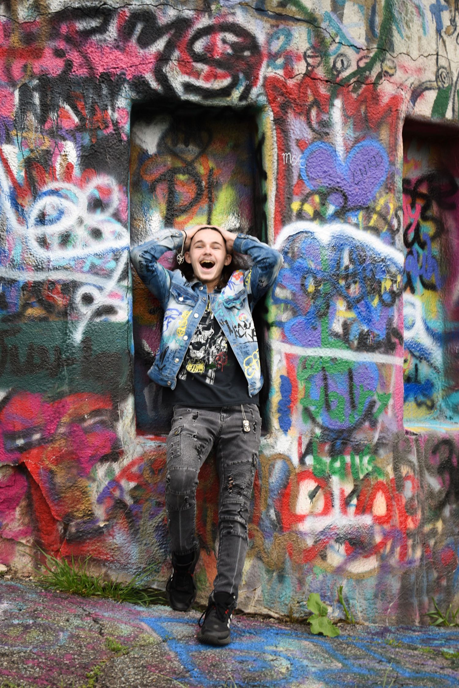 Energetic pose against vibrant graffiti wall while wearing denim jacket.