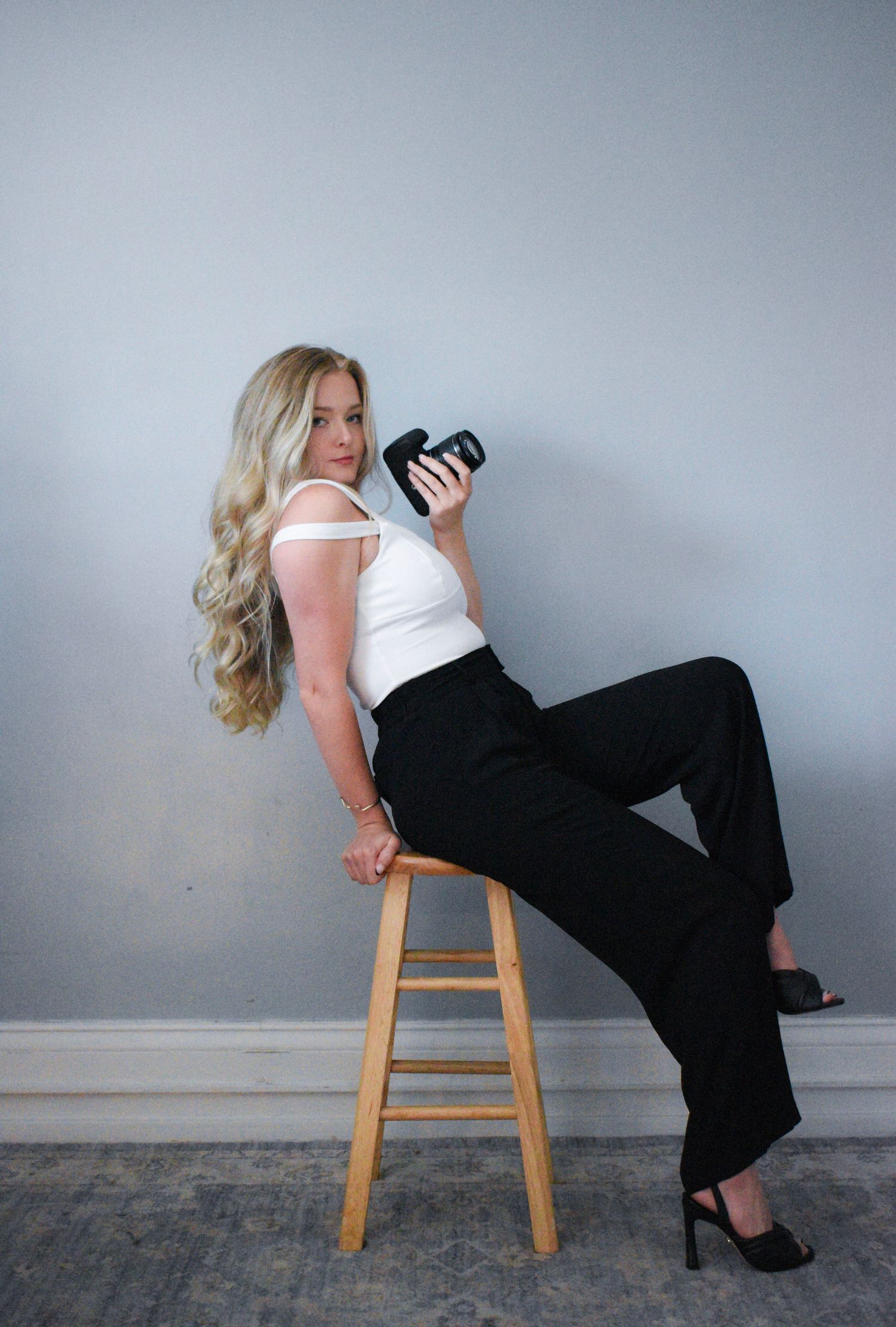 A creative photoshoot featuring someone posing on a wooden stool against a gray wall.