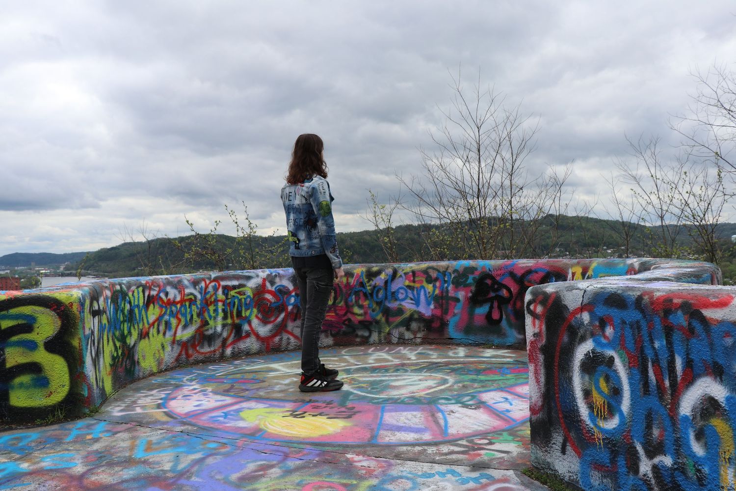 Standing on graffiti-covered lookout point with cloudy mountain vista.
