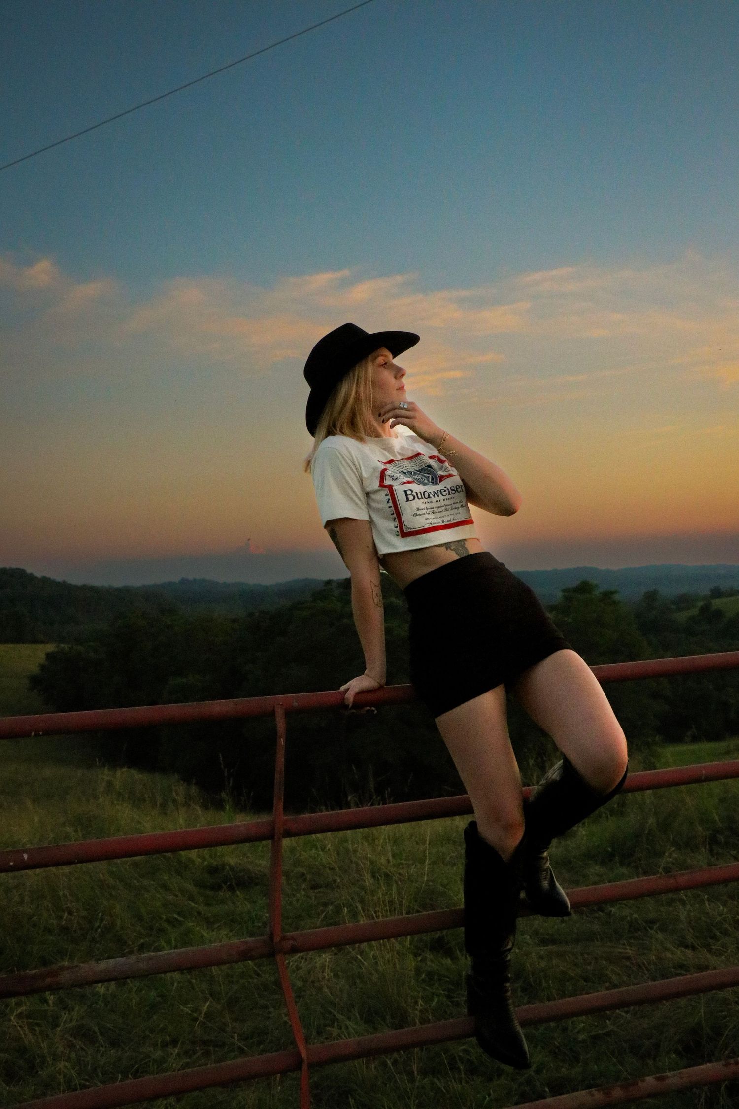 Person seated on rustic wooden fence against scenic sunset mountain backdrop.