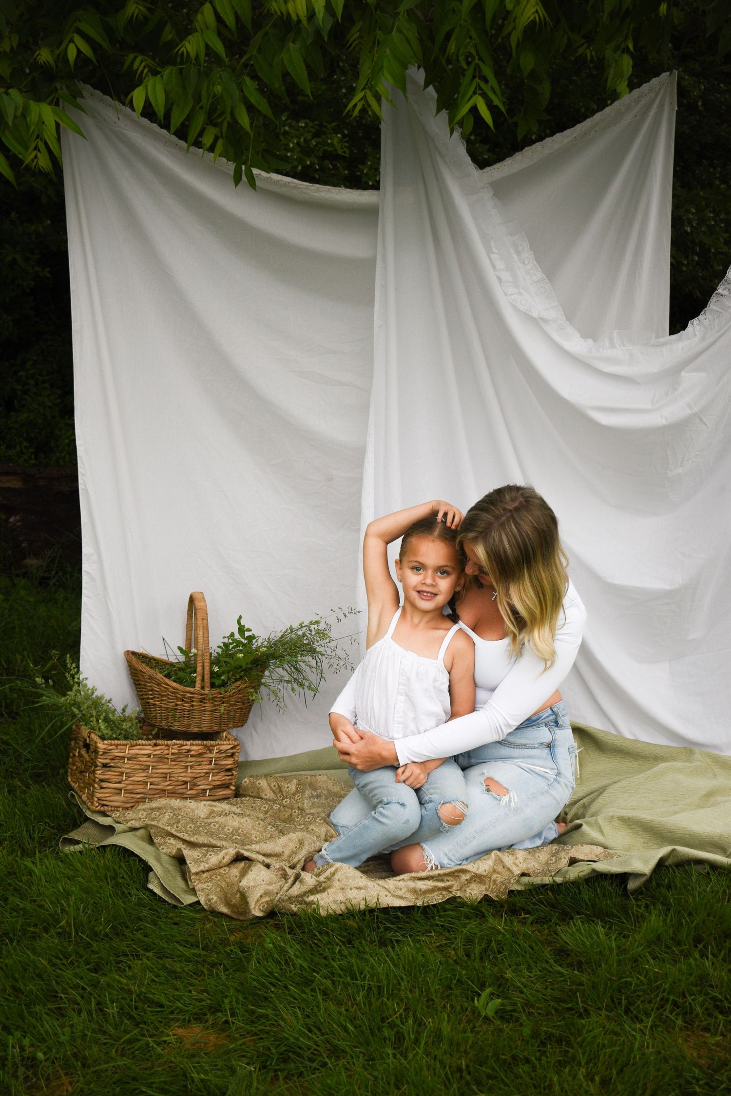 Family photoshoot setup with white backdrop, wicker basket and burlap blanket on grass.