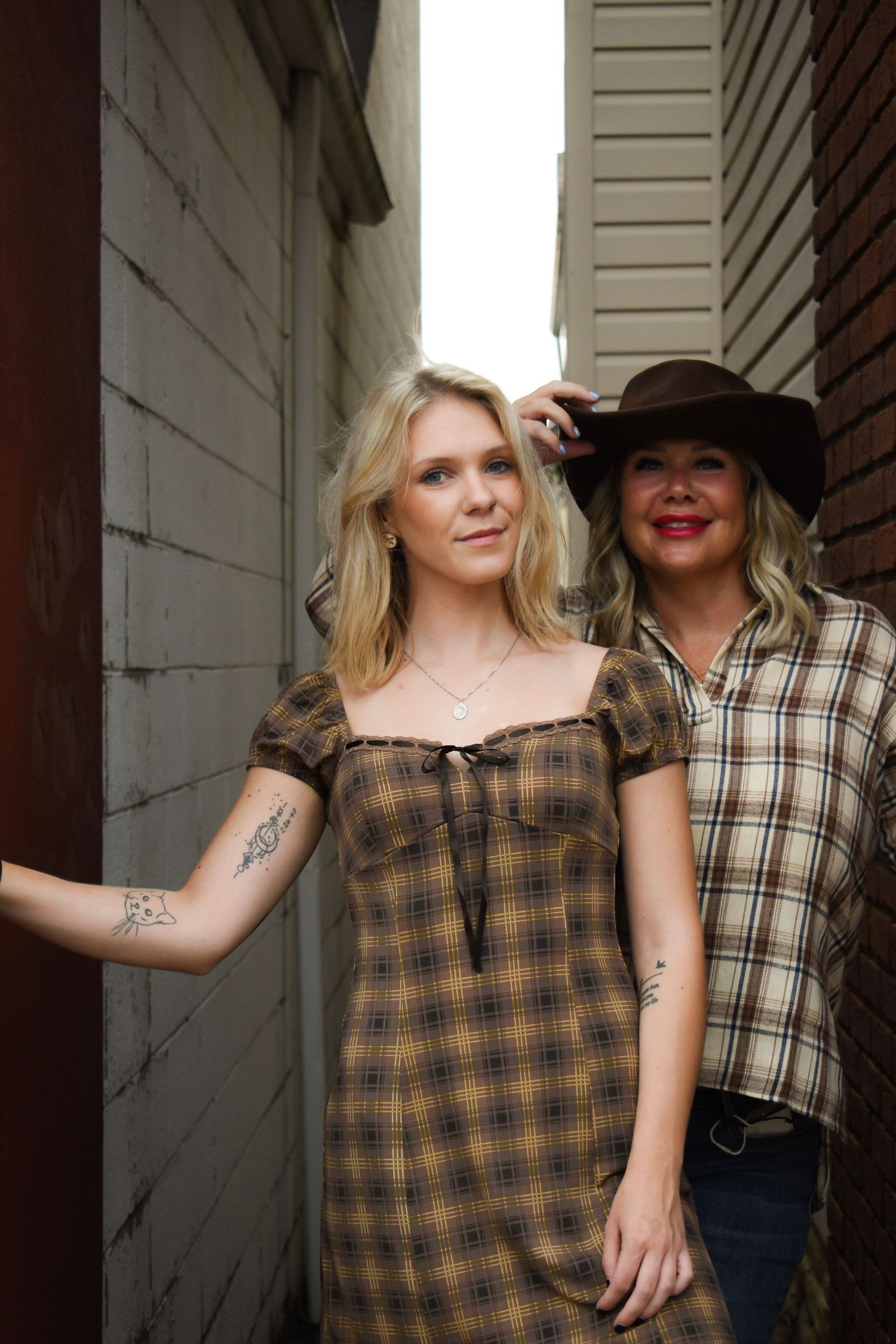 Two people posing in a narrow alleyway wearing country-inspired fashion.