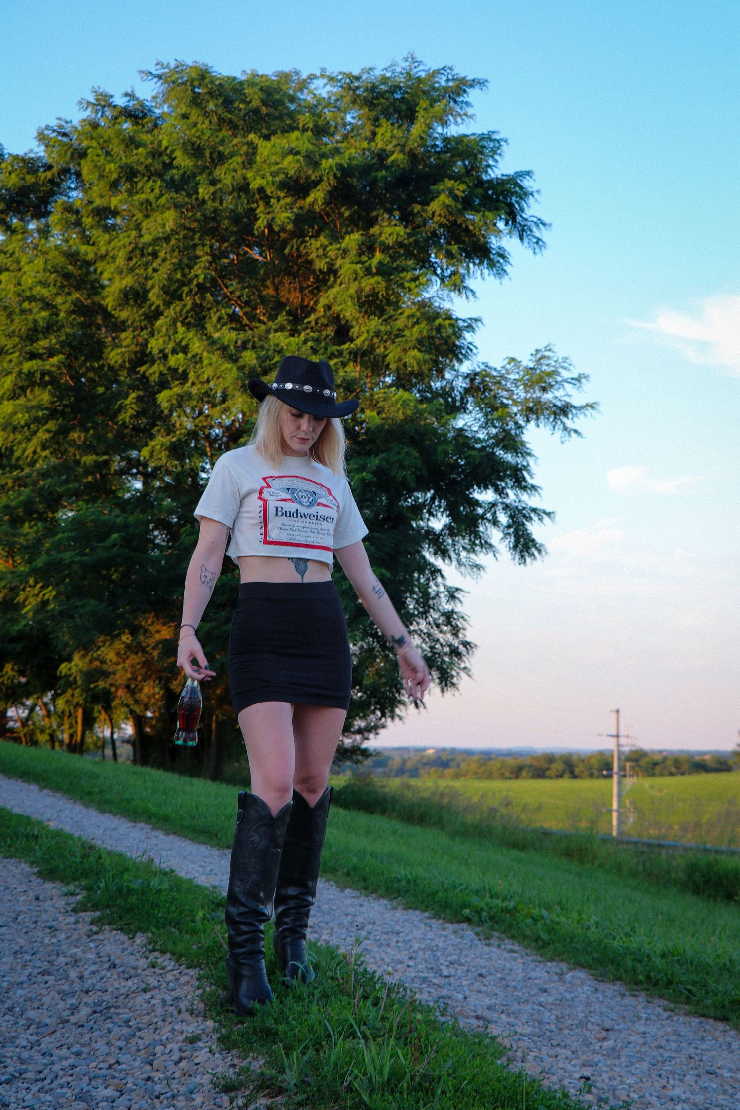 Person in black boots walking on a gravel path with green grass and trees in the background.