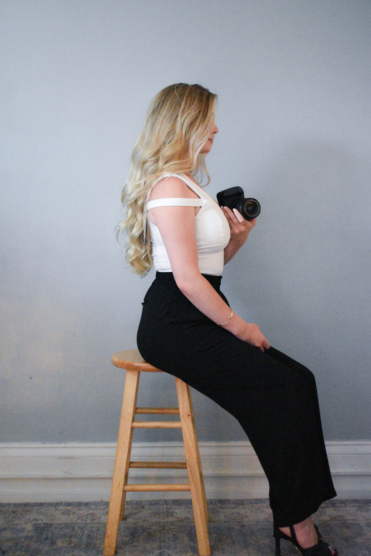Side profile studio portrait of person in white top and black pants holding camera.