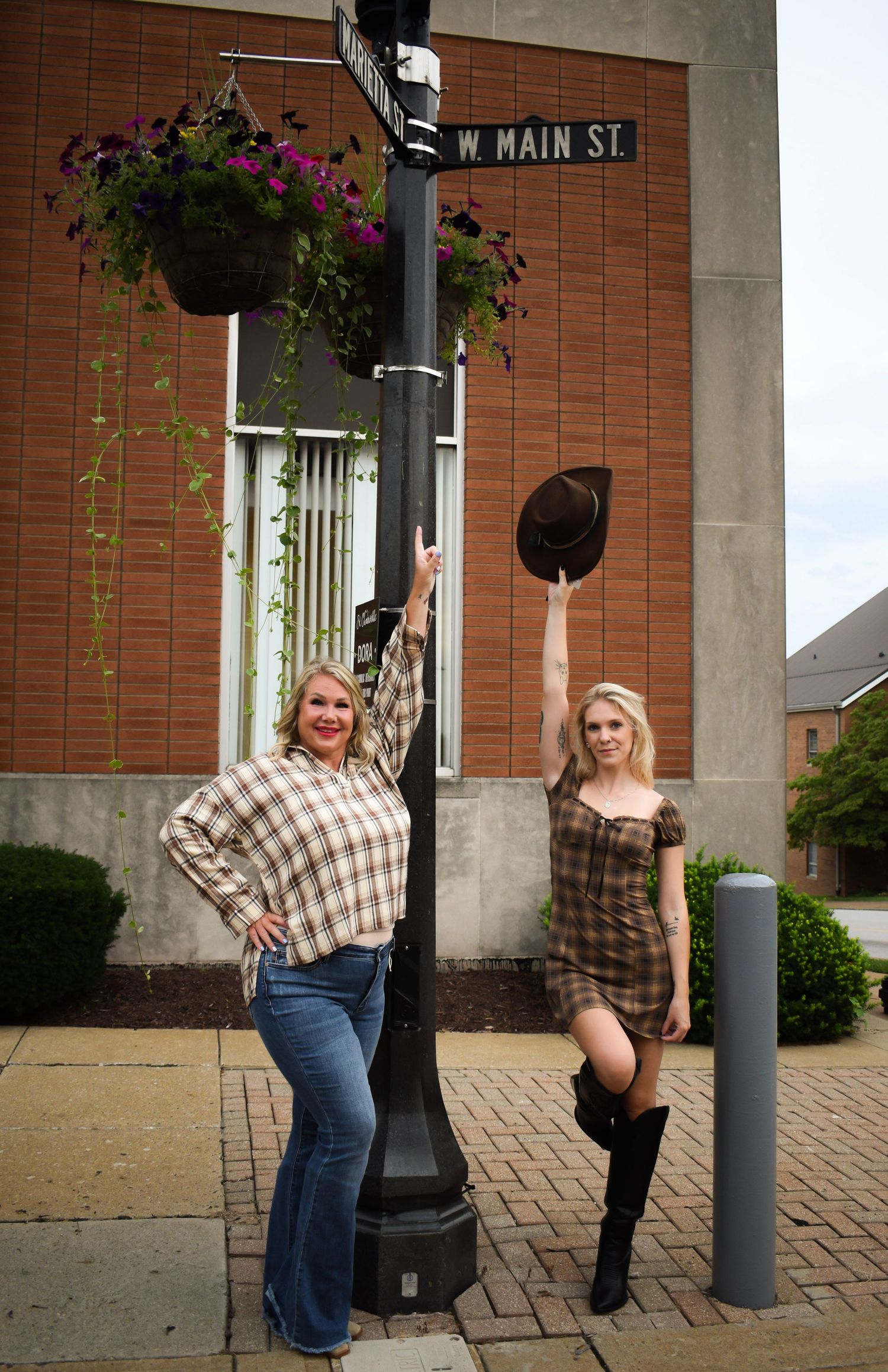Two people pose by a decorative lamppost with hanging flowers on West Main Street.
