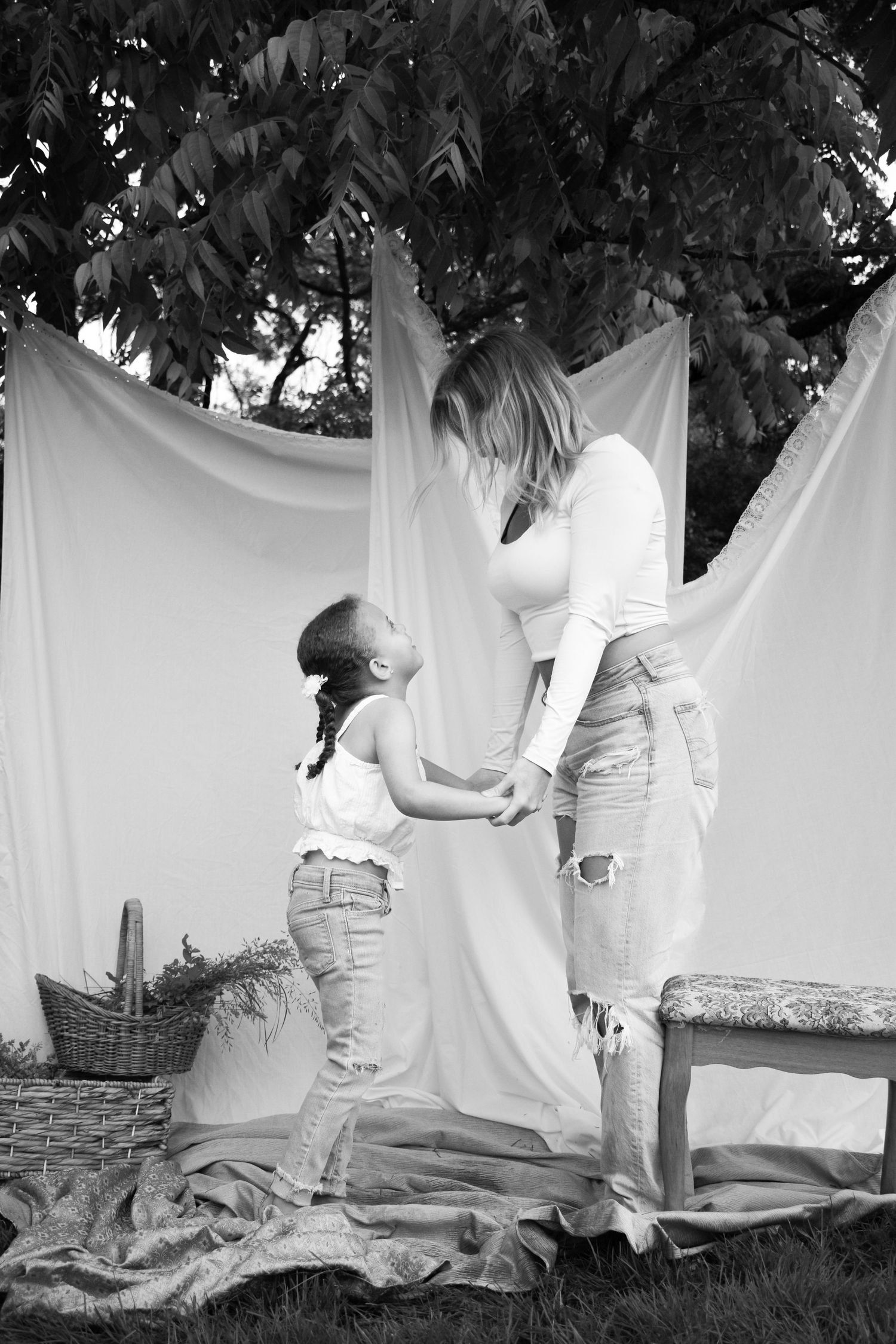 A tender black and white photo of parent and child holding hands against a white backdrop outdoors.