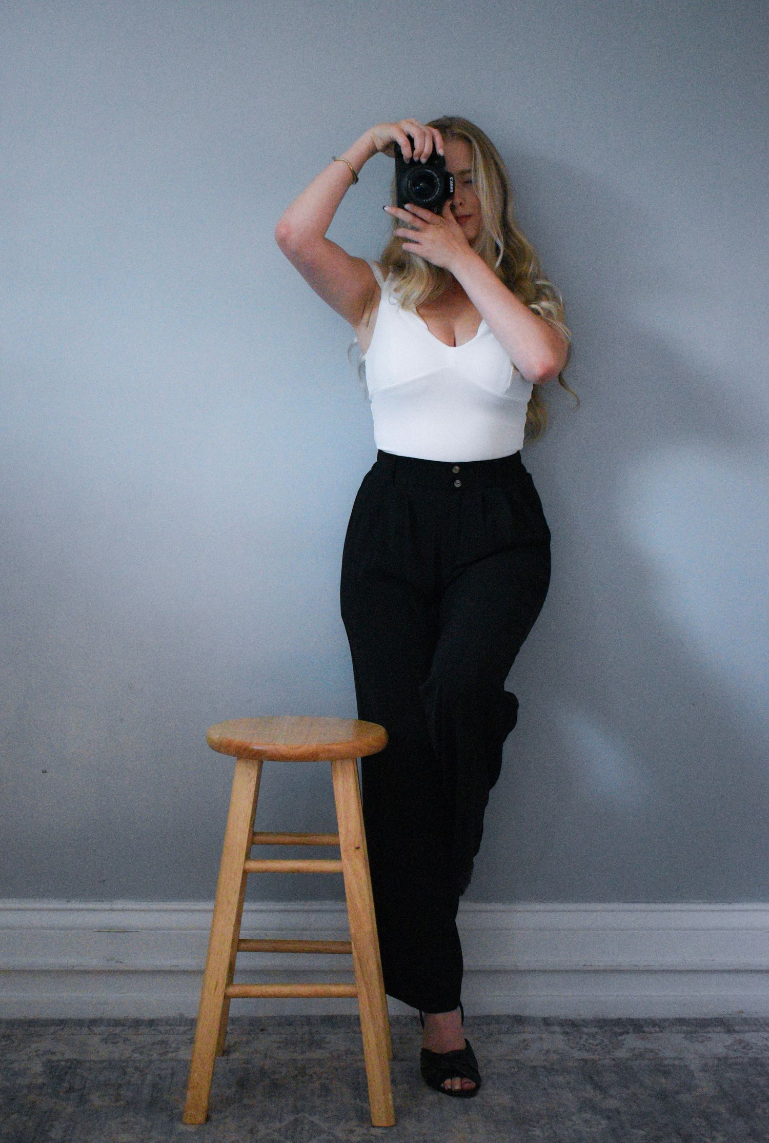 Person in casual attire takes photo with vintage camera beside wooden stool.