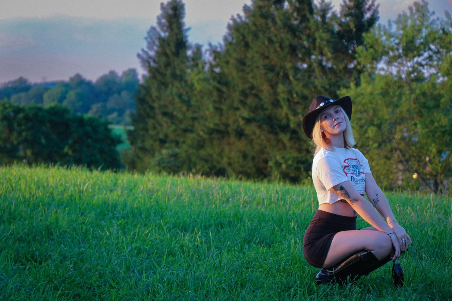Artistic outdoor photoshoot on a grassy hill with mountains and trees in the background.