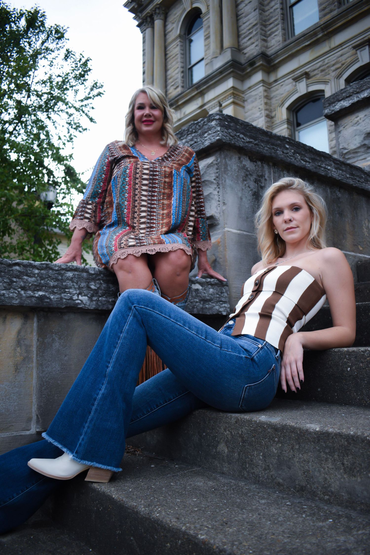 Two people in retro-inspired clothing lounging on concrete steps of a historic building.