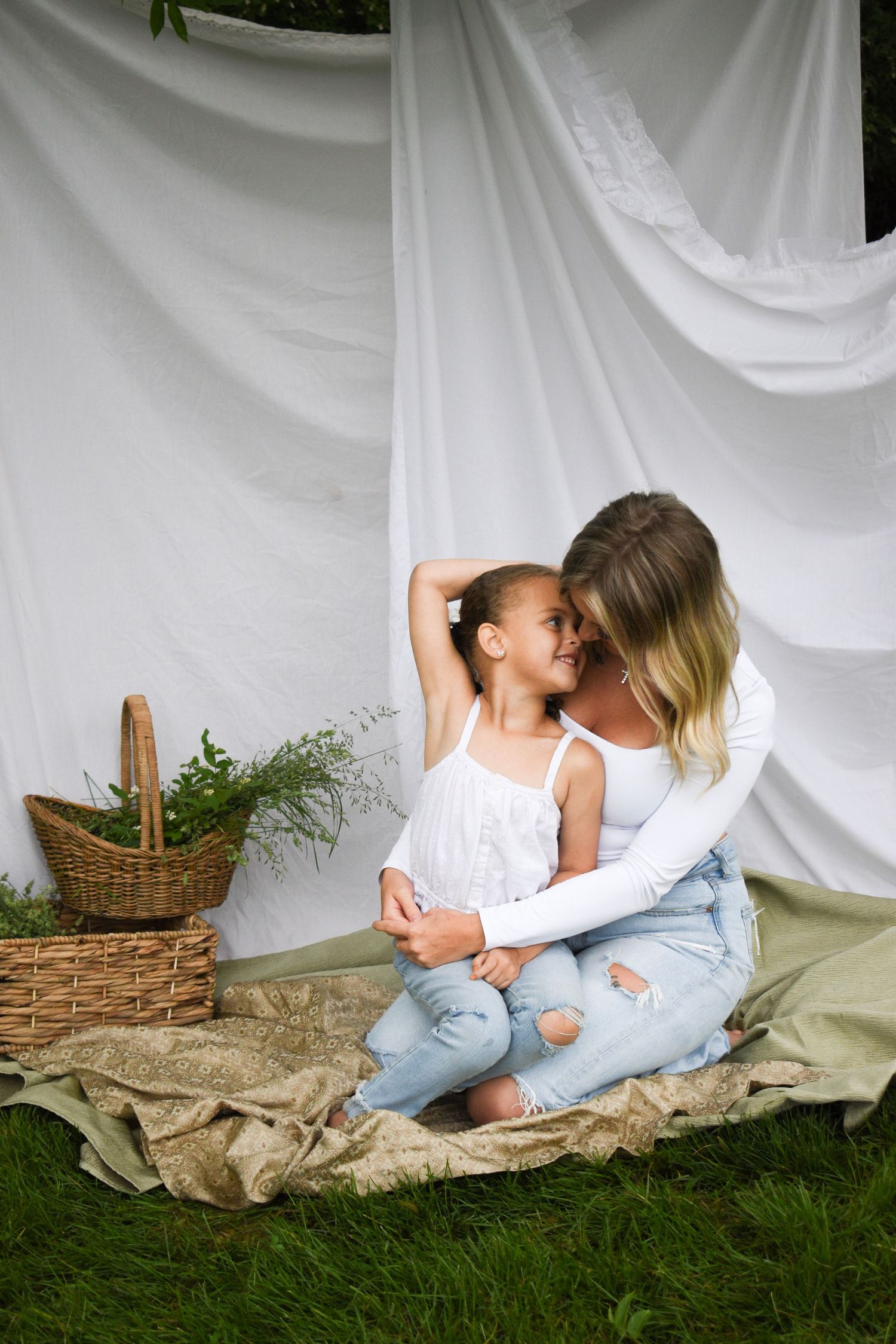 Sweet family moment captured against white backdrop with wicker basket and blanket on grass.
