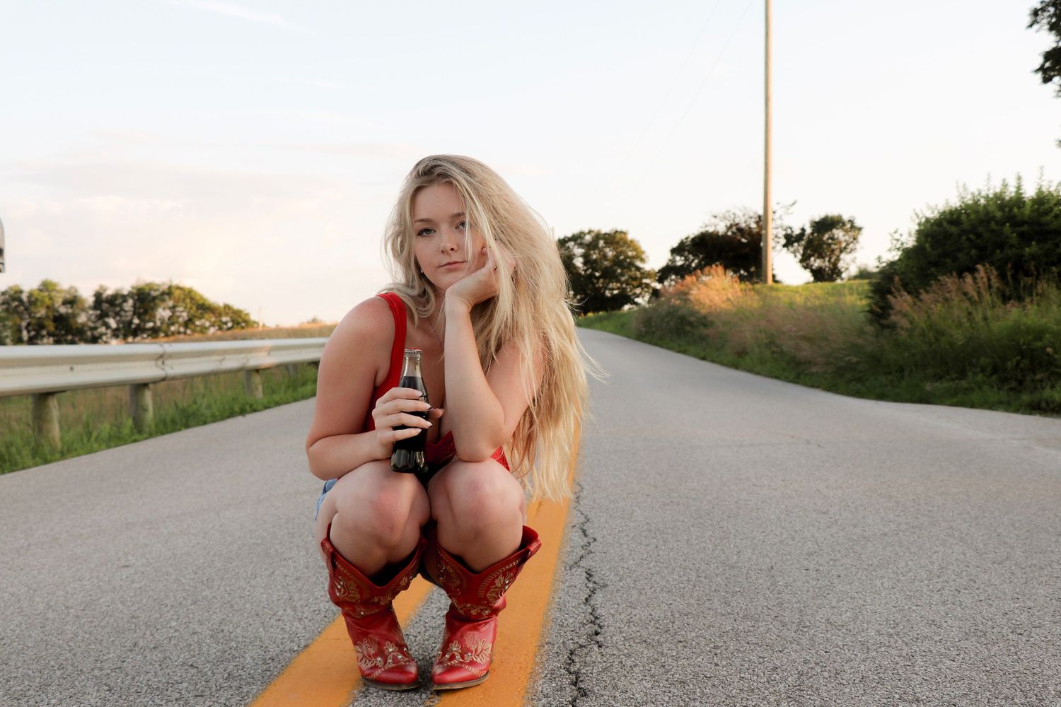 Woman in casual outfit sitting on painted yellow road lines during golden hour.