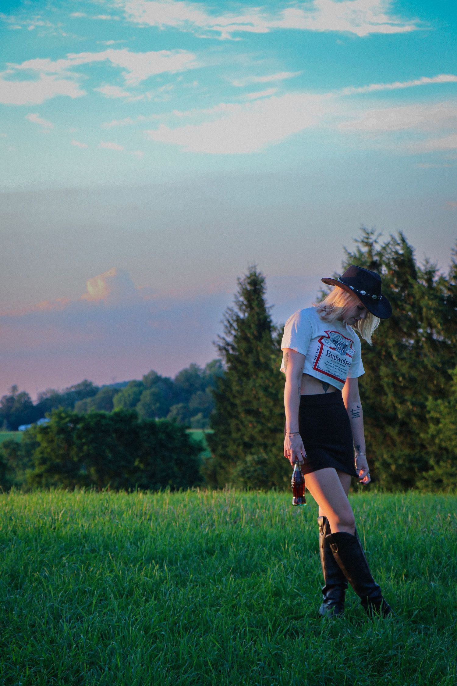 Person in casual attire standing in green meadow under bright blue summer sky.