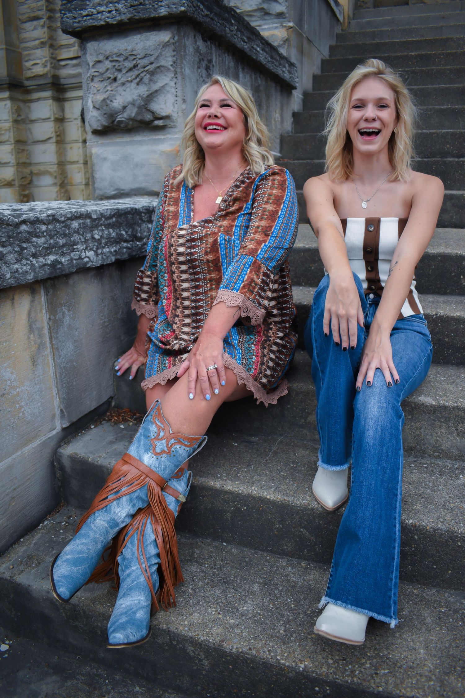 Two people laughing together on stone steps wearing bohemian and casual western styles.