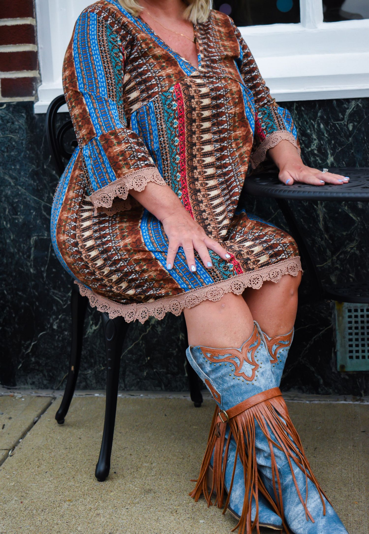 Close-up of ornate blue fringe boots and patterned boho dress while sitting outdoors.