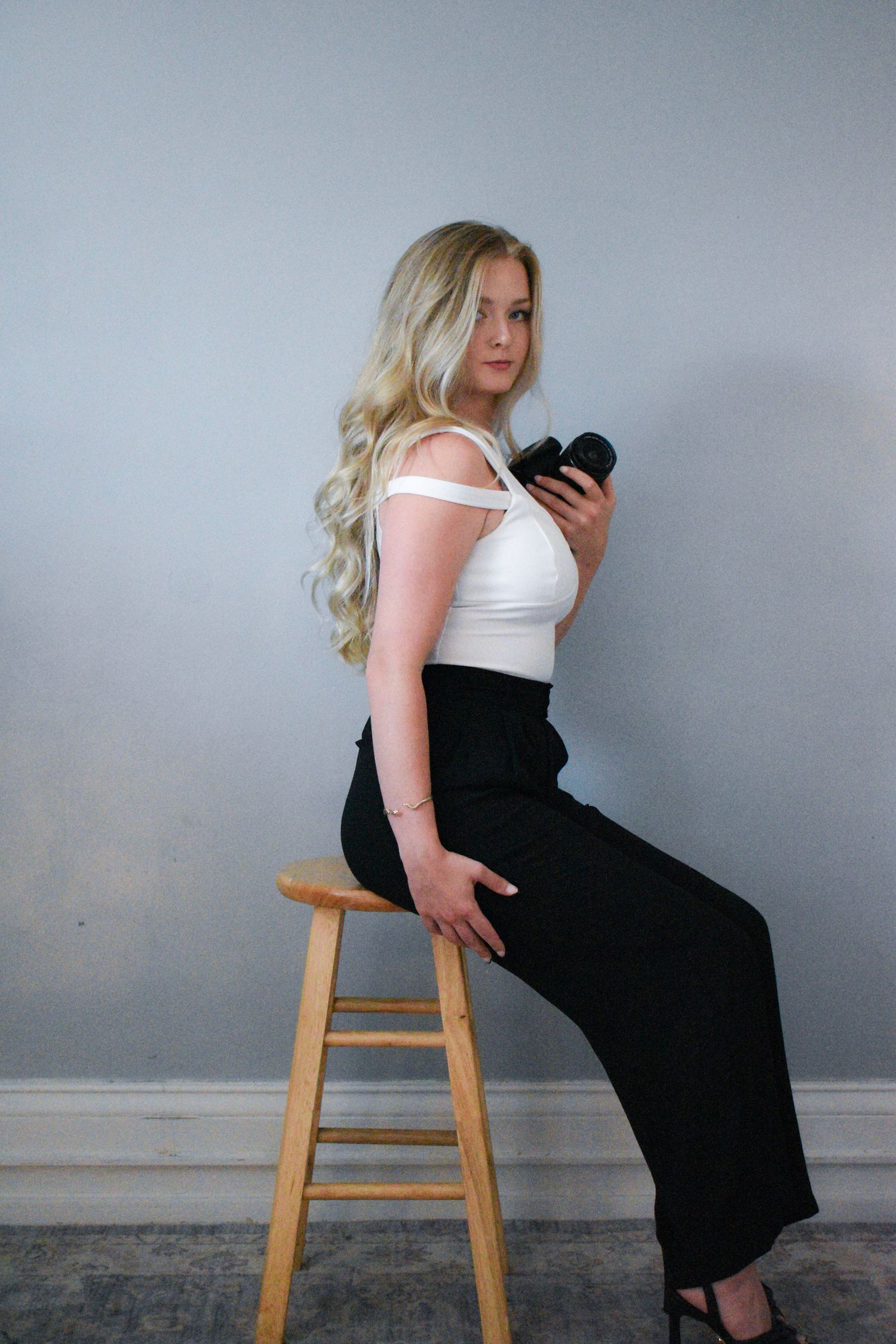 Studio fashion portrait featuring white top and black pants with camera as prop.