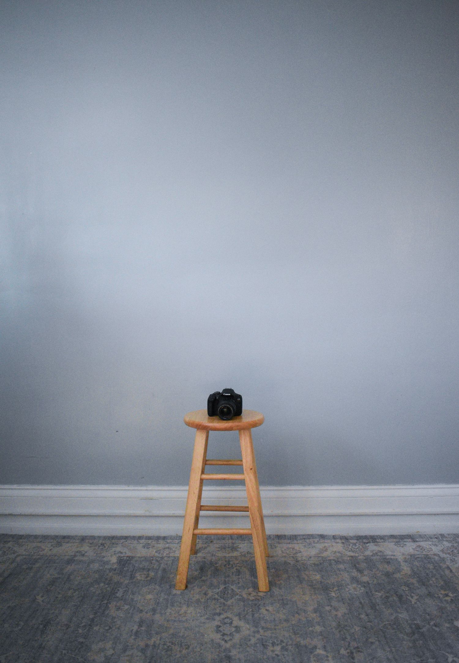 Black camera sitting alone on wooden stool against grey wall.