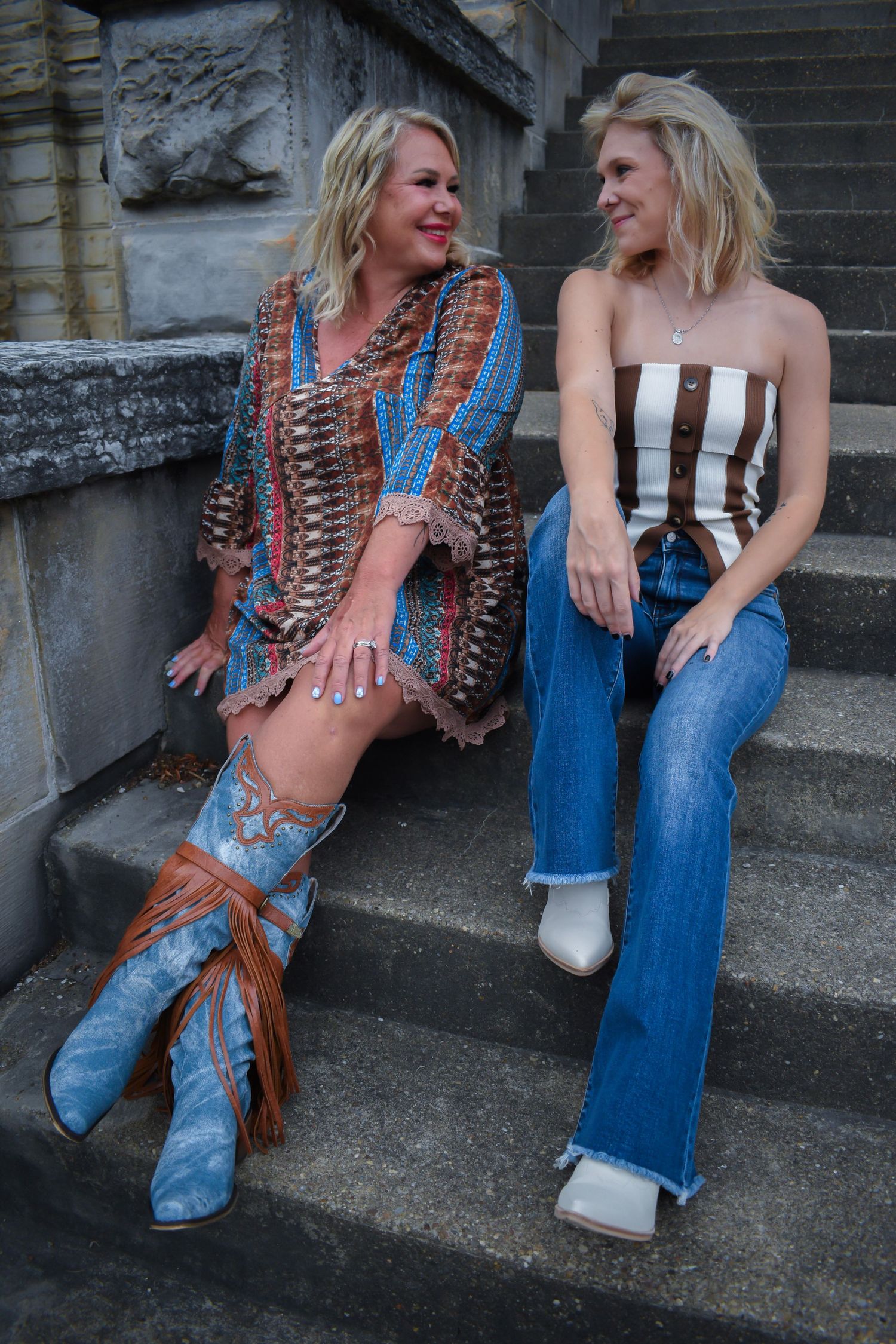 Two people in western and casual wear sitting on stone steps sharing a laugh.