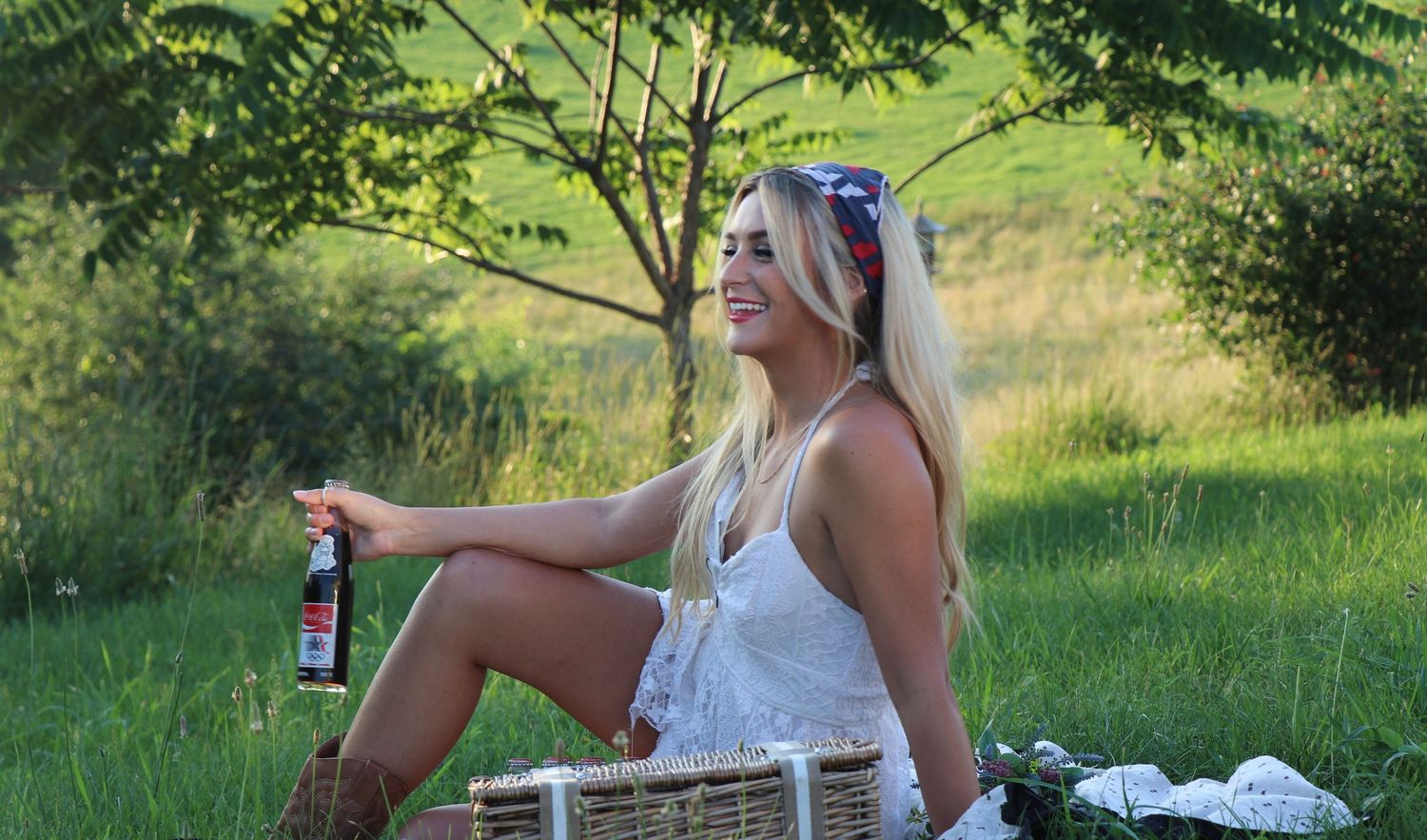 Summer picnic scene with white dress and beverage against green hillside backdrop.