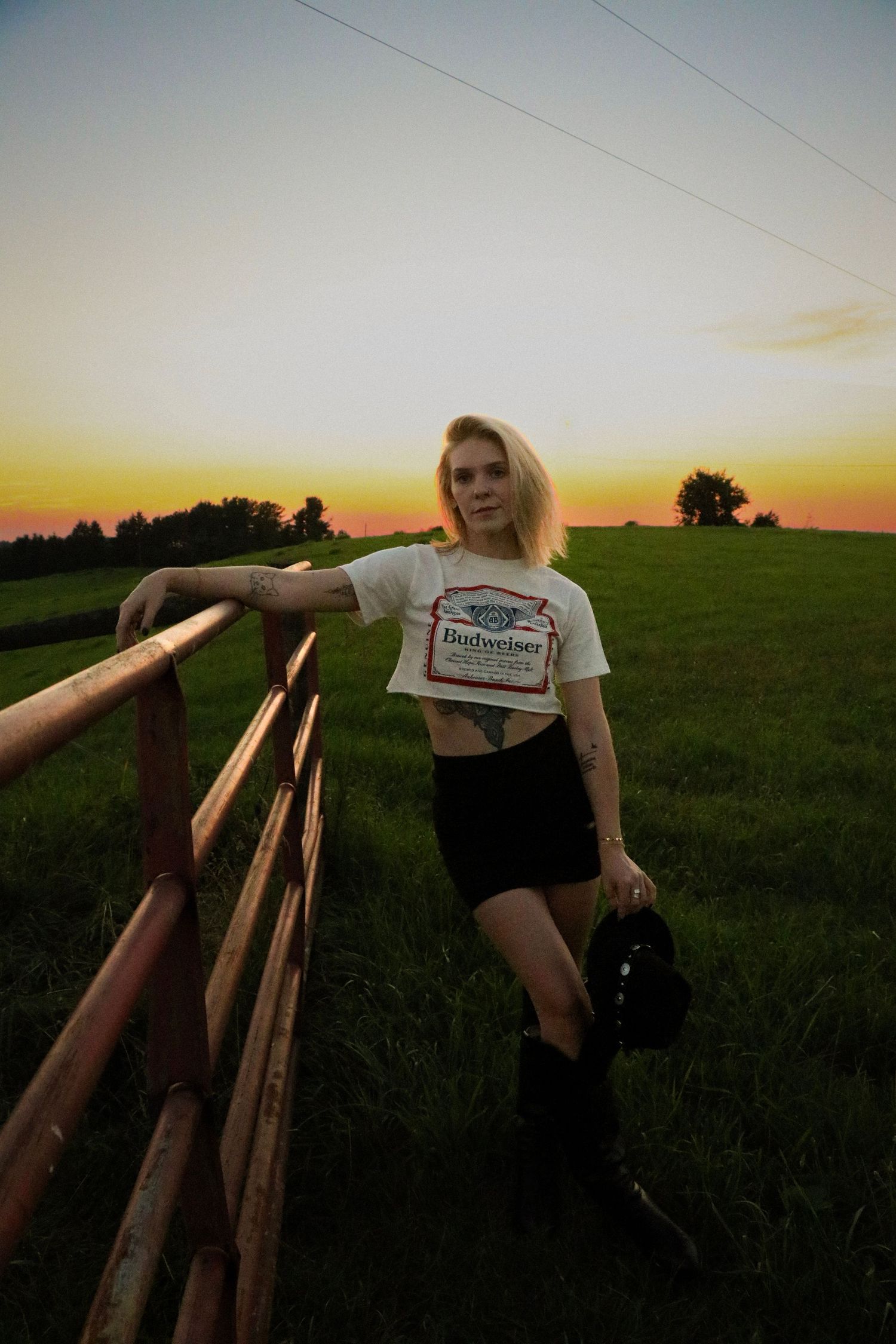 Country sunset photoshoot featuring casual summerwear and a wooden fence in a rural field setting.