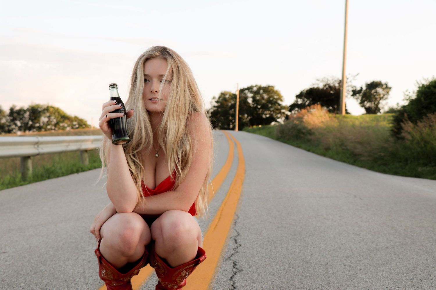 Person in red top sitting on yellow road lines at sunset.